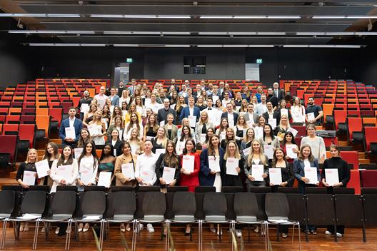Ein Gruppenfoto der Graduierten im Audimax der HSD. Sie halten ihre Abschlussurkunden in der Hand.
